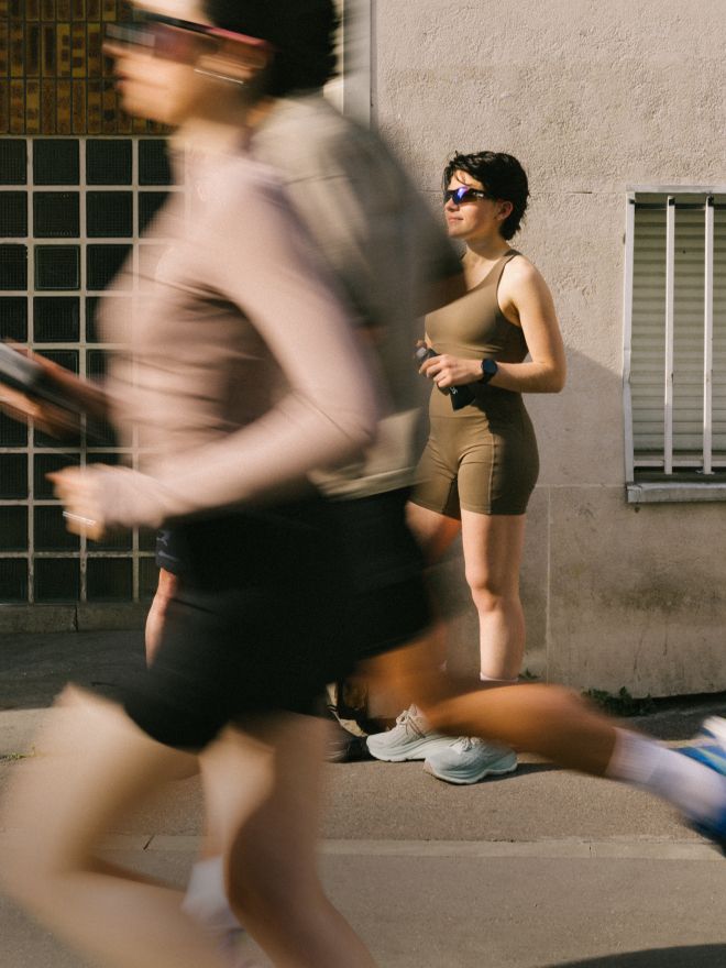 Runners resting by a wall while a runner passes in the foreground